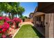 Home's private backyard features an artificial lawn area, bordered by vibrant flowers and mature trees at 14314 W Lexington Ave, Goodyear, AZ 85395