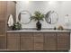 Bathroom featuring wooden cabinets, double sinks, framed circular mirrors, and decorative greenery at 26943 N 74Th Ave, Peoria, AZ 85383