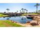 Beautiful community pond with stone bridge, palm trees, lush green grass, and sparkling blue water under a clear sky at 35990 N Desert Tea Dr, Queen Creek, AZ 85140