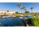 Scenic pond with flowing water, palm trees, lush landscaping, and a glimpse of a building under a clear blue sky at 35990 N Desert Tea Dr, Queen Creek, AZ 85140