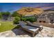 Relaxing backyard featuring an outdoor fireplace, travertine patio, and two lounge chairs under a large umbrella at 21275 E Russet Rd, Queen Creek, AZ 85142