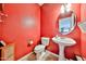 Bathroom featuring a pedestal sink, round mirror, and a classic white toilet against red painted walls at 15040 W Windrose Dr, Surprise, AZ 85379