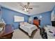 Bedroom with blue walls, ceiling fan, a cozy bed, dresser, and desk setup at 15040 W Windrose Dr, Surprise, AZ 85379