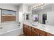 Main bathroom featuring double sinks, soaking tub, window with blinds, and access to the walk-in closet at 16118 W Port Au Prince Ln, Surprise, AZ 85379