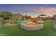 Stunning backyard with a pool, fire pit, and lush landscaping perfect for outdoor entertaining in the evening at 18199 W Buckhorn Dr, Goodyear, AZ 85338