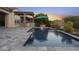 Beautiful pool with a waterfall feature, outdoor kitchen, a fire pit, and green foliage at 20595 W Pasadena Ave, Buckeye, AZ 85396