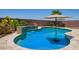 Inviting pool with a waterfall feature, surrounded by a decorative stone patio, lush landscaping, and a shade umbrella at 25546 N 164Th Dr, Surprise, AZ 85387