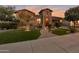 Charming home with lush green lawn, stone accents, and a paver walkway leading to a well-lit entrance under a colorful sunset at 3907 E Carob Dr, Gilbert, AZ 85298