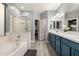 Bright bathroom features a soaking tub, glass shower, double vanity with blue cabinets, and a walk-in closet at 13636 W Calavar Rd, Surprise, AZ 85379