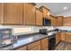 This kitchen has wooden cabinets and granite countertops, with black appliances and wood-style flooring at 23886 W Harrison Dr, Buckeye, AZ 85326