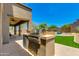 Outdoor kitchen and barbecue area, perfect for entertaining, overlooks the lush green lawn and pool at 3804 E Daley Ln, Phoenix, AZ 85050