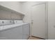 Functional laundry room with full-size washer, dryer, storage shelf and neutral colors at 43938 W Colby Dr, Maricopa, AZ 85138