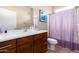 Bathroom with wood cabinets, white countertops, large vanity mirror, and a toilet with a purple shower curtain at 6745 N 93Rd Ave # 1129, Glendale, AZ 85305