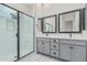 Modern bathroom with a double vanity, gray cabinetry, and a glass-enclosed shower with white subway tile at 17322 W Puget Ave, Waddell, AZ 85355
