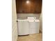 Well-lit laundry room features a white washer and dryer beneath brown cabinets and beige tiled floor at 4224 E Renee Dr, Phoenix, AZ 85050