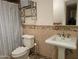 A tiled bathroom featuring a toilet, sink, mirror, decorative shelf, and shower at 211 Bahia E Ln, Litchfield Park, AZ 85340