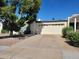 A beige house with a two-car garage and a large tree in the front yard at 211 Bahia E Ln, Litchfield Park, AZ 85340