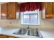 Kitchen featuring a stainless steel double sink, white countertops and wooden cabinets beneath a window with red accents at 7531 W Kimberly Way, Glendale, AZ 85308