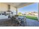 A covered outdoor kitchen and dining area features a stainless grill, marble backsplash, and lush backyard view at 11250 W Prospector Dr, Queen Creek, AZ 85144
