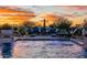 Backyard pool with water features, lounge seating, and lush landscaping under a colorful sunset sky at 11250 W Prospector Dr, Queen Creek, AZ 85144