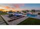Backyard oasis featuring a sparkling pool, outdoor seating, fire pit, and lush landscaping under a vibrant sunset sky at 11250 W Prospector Dr, Queen Creek, AZ 85144