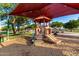 Community playground with colorful play structures, slides, and a protective shade canopy over a soft wood chip surface at 18402 E Oak Hill Ln, Queen Creek, AZ 85142
