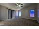 A large bedroom with a ceiling fan, plush carpet, multiple windows, and vertical blinds at 25748 W Siesta Way, Buckeye, AZ 85326