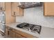 Close-up of modern gas range, stainless steel vent hood, tile backsplash, and wood cabinetry at 16981 W Cameron Dr, Surprise, AZ 85388