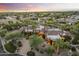 Expansive desert home boasts lush landscaping, a circular driveway, and a unique, turreted design under a colorful sunset sky at 7640 E Poinsettia Dr, Scottsdale, AZ 85260