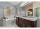 Bathroom featuring a dual sink vanity, framed mirror, glass block window, tub and walk-in shower at 10235 E Jerome Ave, Mesa, AZ 85209