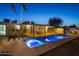 Inviting backyard oasis featuring a sparkling pool, spa, covered patio with seating, and lush landscaping at twilight at 421 N Evergreen St, Chandler, AZ 85225