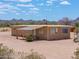 A charming tan single-story house with a metal roof sits on a vast desert landscape at 270 S Ralston Rd, Maricopa, AZ 85139