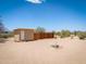 Exterior view of a tan shed with a white door nestled on a dirt lot under a bright blue sky at 270 S Ralston Rd, Maricopa, AZ 85139