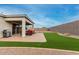 Wide backyard with a covered patio, BBQ grill, artificial grass, and desert landscaping at 17721 W Sandalwood Dr, Goodyear, AZ 85338