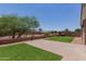Backyard featuring a well maintained lawn, brick patio, and a metal fence. Tree provides shade, enhancing the outdoor experience at 41041 W Somers Dr, Maricopa, AZ 85138