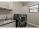 This laundry room features a sink, gray countertops and cabinets, plus a modern black washer and dryer at 20452 E Appaloosa Dr, Queen Creek, AZ 85142