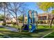 View of the blue playground on a green lawn with shady trees, a bench, and homes behind it at 2063 S Edgewater --, Mesa, AZ 85209