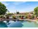Backyard with a view of sparkling pool with lush landscaping, mature trees, and water view beyond the wrought iron fence at 6376 W Louise Dr, Glendale, AZ 85310