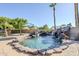 Backyard swimming pool with rock waterfall feature and lush landscaping with clear blue sky at 12434 S Ki Cir, Phoenix, AZ 85044