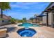 Beautiful pool and spa with custom tile work, surrounded by a stone patio and lush landscaping, ideal for relaxation at 18455 W San Carlos Dr, Goodyear, AZ 85338