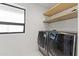 Modern laundry room with sleek black washer and dryer units, natural wood shelving, and bright natural light at 1861 W Navarro Ave, Mesa, AZ 85202