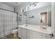 Bathroom featuring dual sinks, white cabinets, and a shower with a tub and shower curtain at 18203 W Port Royale Ln, Surprise, AZ 85388