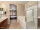 A primary bathroom featuring a tub, glass-enclosed shower, and an arched doorway to the main bedroom at 44517 W Copper Trl, Maricopa, AZ 85139