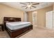 A neutral bedroom featuring a dark wood bed frame, a ceiling fan, and an en-suite bathroom at 44517 W Copper Trl, Maricopa, AZ 85139