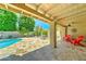 Inviting covered patio with travertine flooring, ceiling fan, red Adirondack chairs, and pool access at 5431 E Piping Rock Rd, Scottsdale, AZ 85254