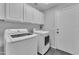 A laundry room with white front load washer and dryer with overhead cabinets and door to the garage at 18088 W San Alejandro Dr, Goodyear, AZ 85338