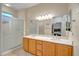 Bright bathroom featuring double sinks, wood cabinets, a large mirror, and a glass door shower at 15314 W Pantano Dr, Surprise, AZ 85374