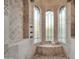 Walk-in shower featuring elegant travertine, bronze fixtures, seating, and arched windows at 8024 E Lone Mountain Rd, Scottsdale, AZ 85266
