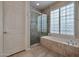 Bright bathroom featuring tile flooring, glass shower, and a soaking tub with shuttered windows at 15634 S 31St St, Phoenix, AZ 85048