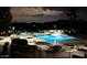 Night view of a lit outdoor pool featuring lounge chairs, umbrellas, and manicured landscaping at 4303 E Cactus Rd # 128, Phoenix, AZ 85032